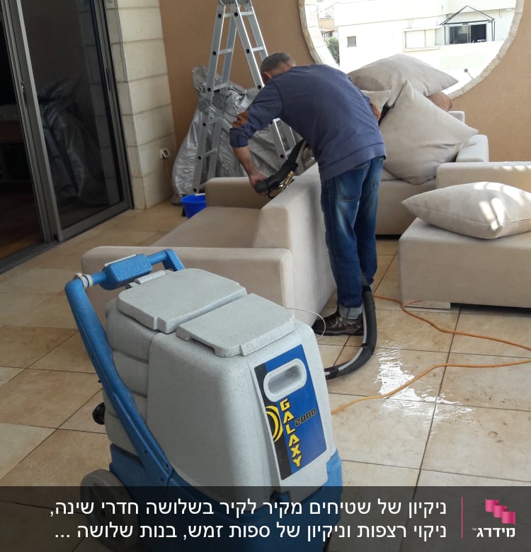 אדם מנקה ספה עם מכונת ניקוי מקצועית